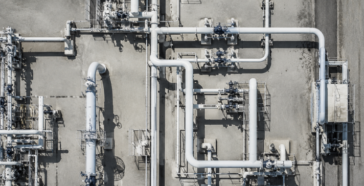 Overhead black-and-white aerial view of an industrial facility showing an intricate network of pipes, valves, and processing equipment