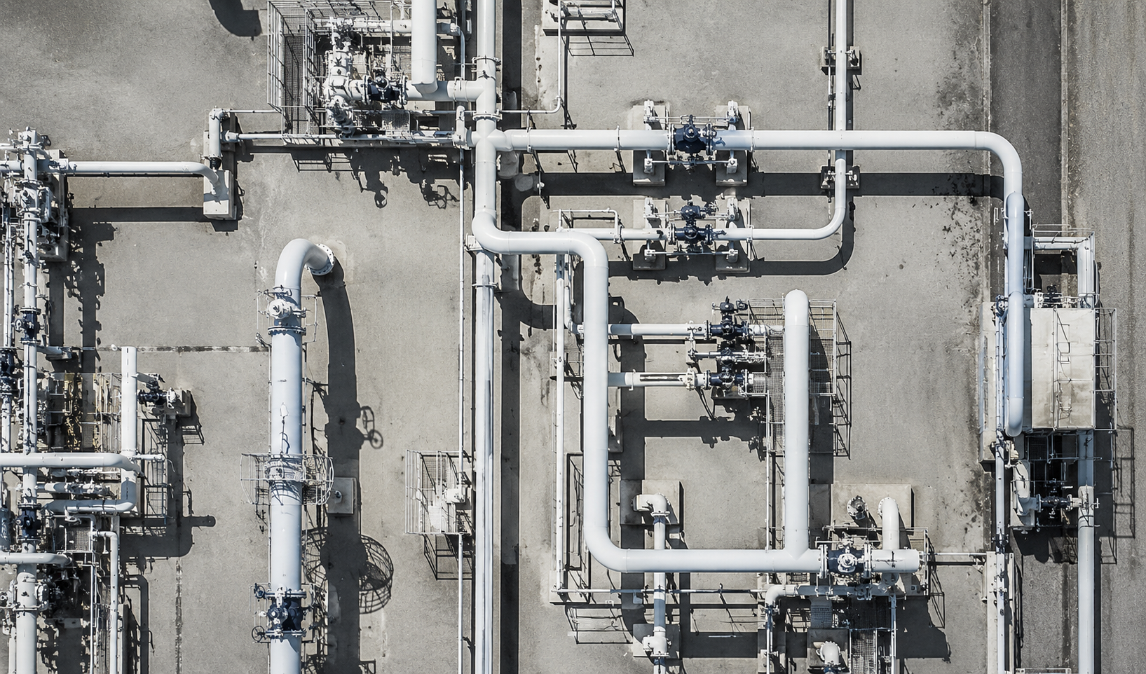 Overhead black-and-white aerial view of an industrial facility showing an intricate network of pipes, valves, and processing equipment
