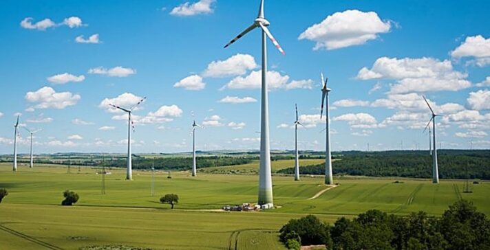 Wind turbines spread across green farmland under a bright blue sky, representing long-term energy infrastructure investment planning
