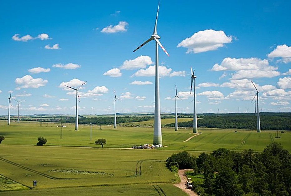 Wind turbines spread across green farmland under a bright blue sky, representing long-term energy infrastructure investment planning