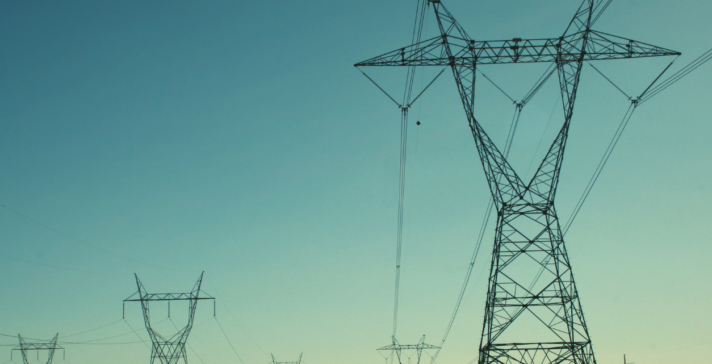 Row of high-voltage electrical transmission towers and power lines receding into the distance against a clear teal-blue sky