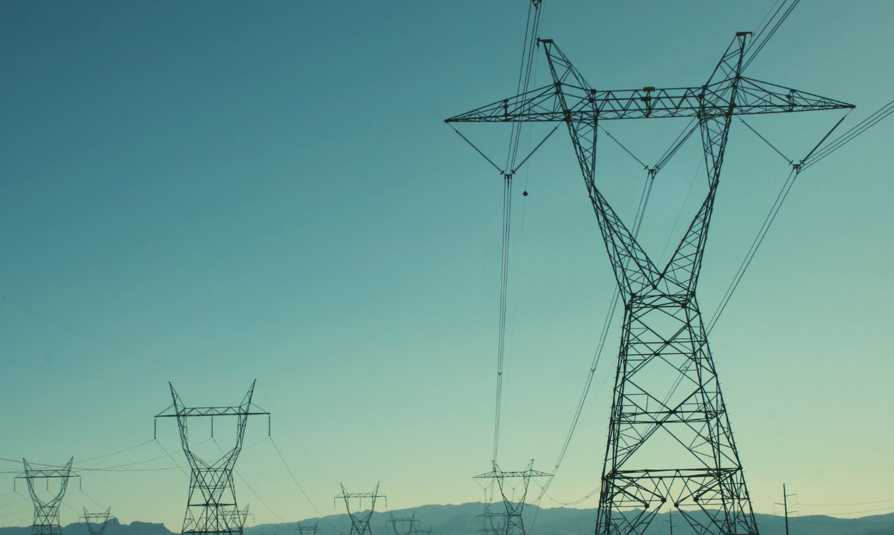 Row of high-voltage electrical transmission towers and power lines receding into the distance against a clear teal-blue sky