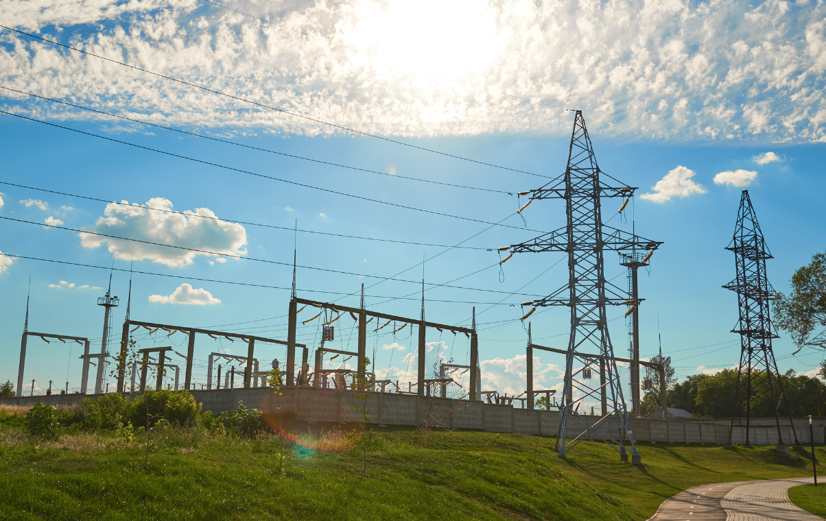 Electrical substation with power lines and transmission towers under a bright blue sky with scattered clouds.