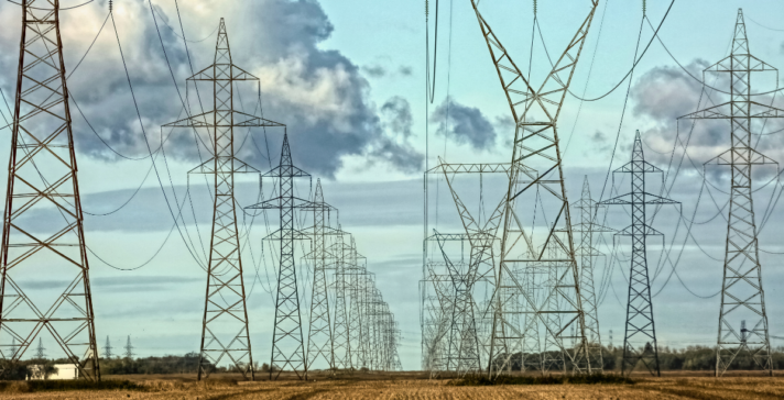 Multiple parallel rows of steel transmission towers carrying high-voltage lines across a harvested field