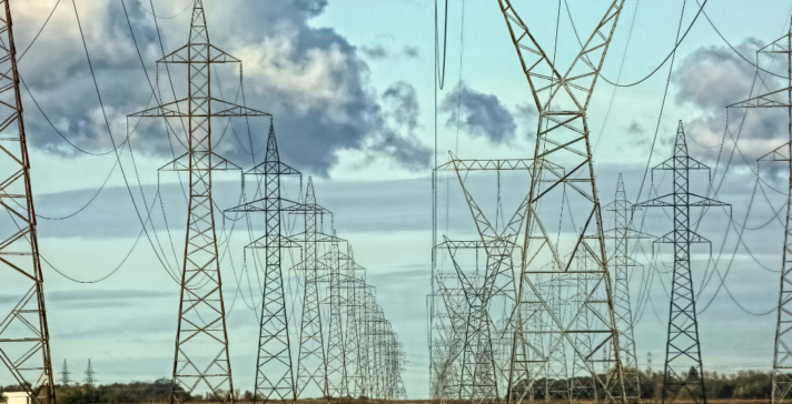 Multiple parallel rows of steel transmission towers carrying high-voltage lines across a harvested field